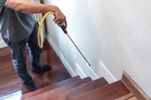 A person shining a flashlight behind a kitchen appliance, inspecting for pest droppings and signs of infestation.